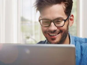 man in glasses looks at a laptop screen