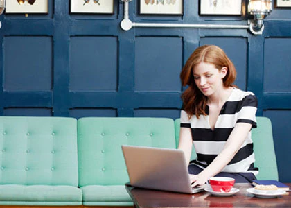 Woman in striped shirt sitting on a teal sofa using her laptop