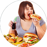 An overweight woman eating and drinking with a pile of burgers in front of her