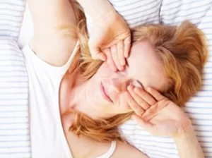 woman waking up in bed and rubbing her eyes with both hands